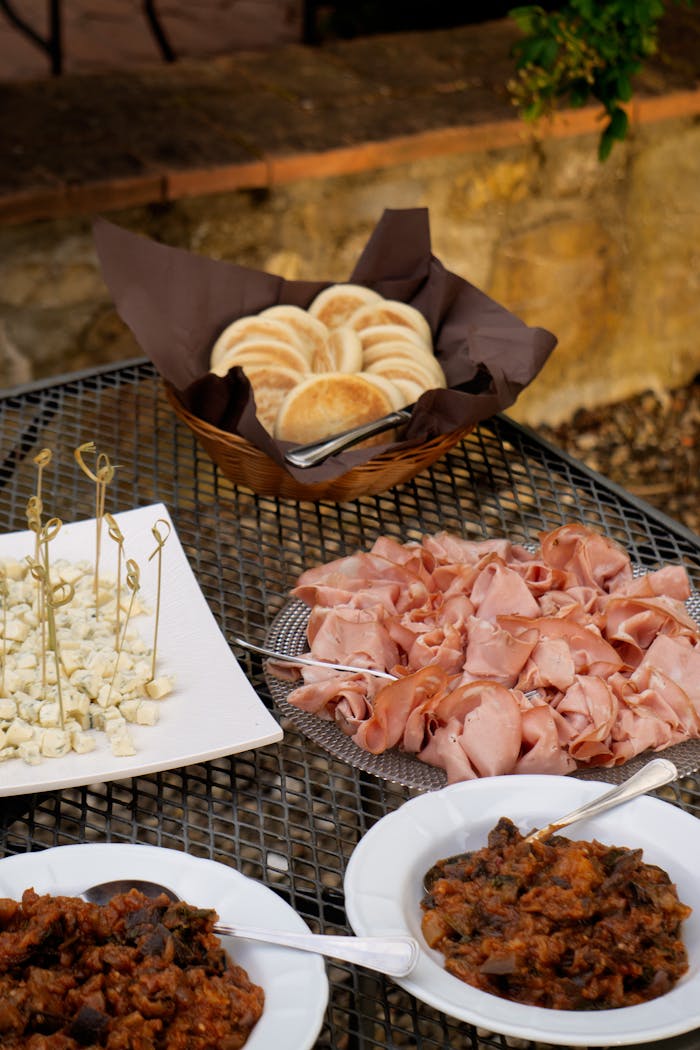 An appetizing spread of cold cuts, bread, and sides on a rustic outdoor table.